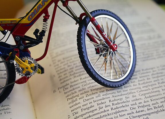 Miniatur-Fahrrad steht auf einem aufgeschlagenen Buch mit deutschem Gesetzestext.