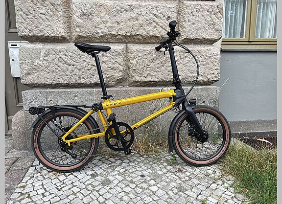 Ahooga E-Max Aufmacher Ein gelb-schwarzes Faltrad steht vor einer Hauswand.