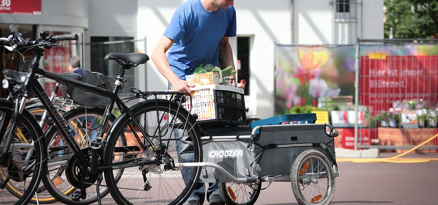 Anhänger Ein Mann belädt einen Fahrradanhänger vorm Supermarkt.